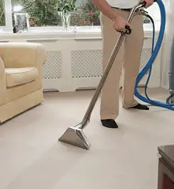 Professional carpet cleaner using a hot-water extraction wand and hose machine in a living room in Tuscaloosa, AL.