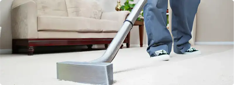 Carpet cleaning technician using a hot-water extraction wand on a light-colored carpet in a living room, Tuscaloosa, AL.