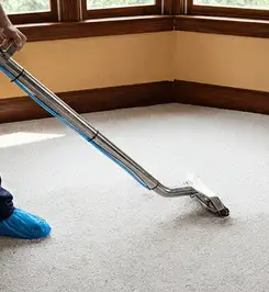 Steam carpet cleaning technician using a hot-water extraction wand on a residential carpet, wearing blue protective shoe covers Tuscaloosa, AL.