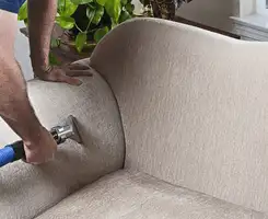 Professional upholstery cleaner deep-cleaning a fabric sofa with a handheld extraction tool and hose in Tuscaloosa, AL.